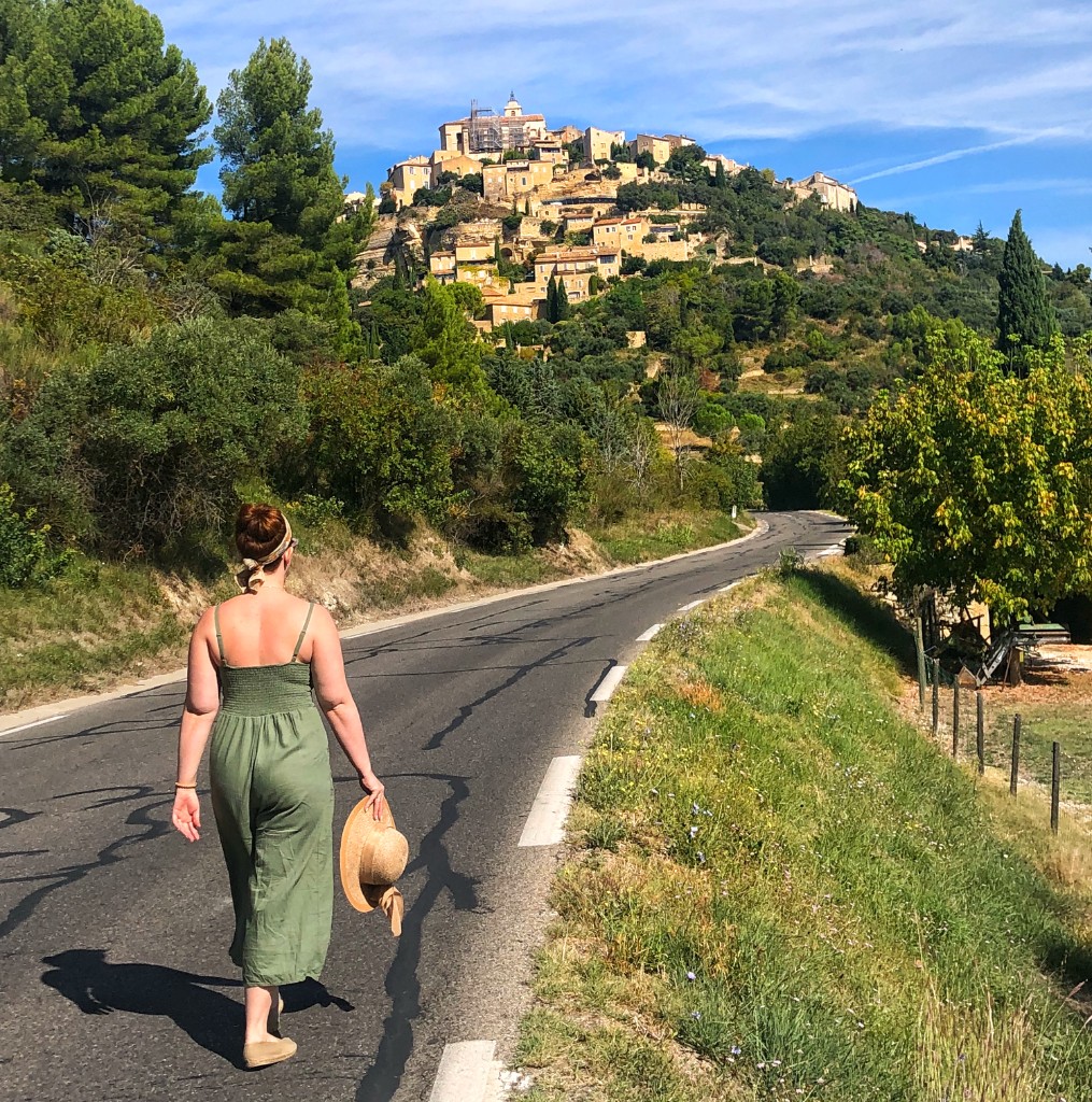A road through Provence toward a hilltop village under a blue sky